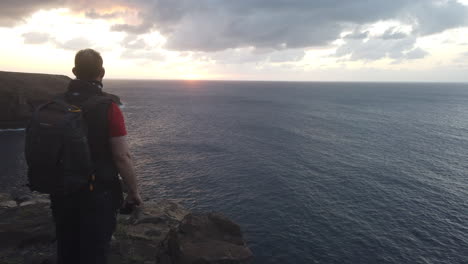 mature-man-with-a-backpack-on-his-back-admires-the-sunset-from-the-cliffs-of-the-coast-of-the-municipality-of-Galdar