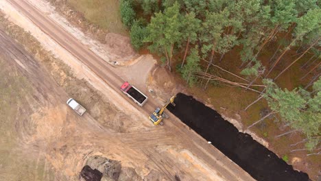 Dump-truck-and-heavy-digger-constructing-gravel-road,-aerial-view