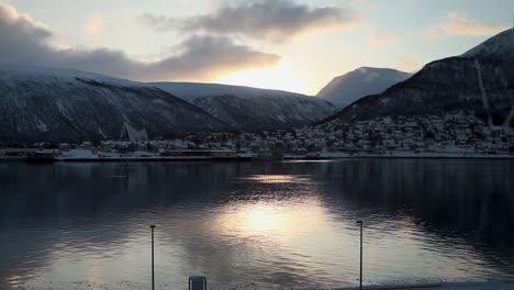Beautiful-static-shot-at-sunset-of-a-sea-with-a-snowy-village-surrounded-by-mountains-reflected-in-the-water