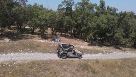 Israel-Army-infantry-squad-soldiers-on-Humvee-vehicle-driving-through-green-field-at-training-ground-country-road,-Aerial-Tracking-shot