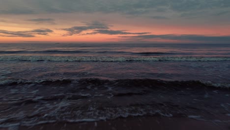 Foamy-ocean-waves-and-orange-sunset-sky,-aerial-fly-backward-view