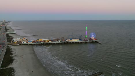 Aerial-view-approaching-the-Galveston-Island-Historic-Pleasure-Pier,-colorful-evening-in-Texas,-USA