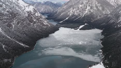 Aerial-view-of-partially-frozen-lake-in-between-snow-frosted-mountain-ranges