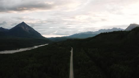 Gigantic-Epic-Drone-Shot-of-Alaskan-Mountain-and-a-car-driving-right-down-the-middle-of-the-road