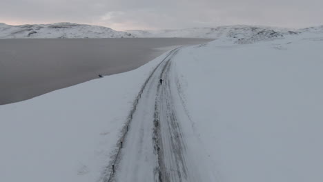 Mujer-Corriendo-En-Un-Camino-Vacío-Y-Helado,-Fondo-De-Montañas,-Islandia-Invernal