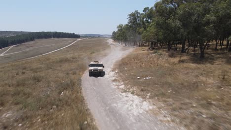 Israel-Army-vehicle-driving-through-green-field-at-training-ground-country-road,-Aerial-Tracking-shot