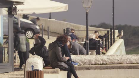 People-sitting-on-wall-in-Nazare-in-Portugal,-typical-day-concept