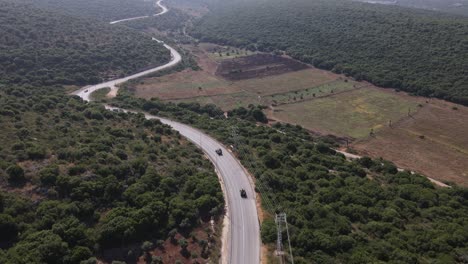 Cinematic-aerial-shot-of-Israel-Army-squad-soldiers-on-vehicles-driving-through-country-road