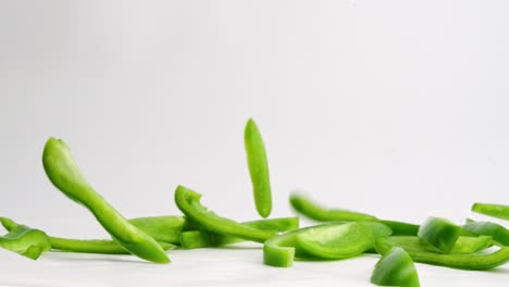 Sliced-green-bell-pepper-pieces-falling-onto-white-table-top-and-bouncing-in-slow-motion