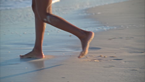Slow-motion-of-a-thin-tanned-woman-legs-walking-on-the-beach-into-the-sea-with-waves-splashing-on-her