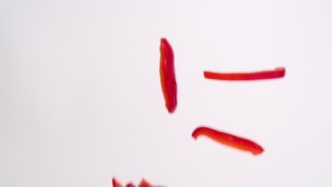 Julienne-cut-sliced-red-bell-pepper-vegetable-pieces-raining-down-on-white-backdrop-in-slow-motion