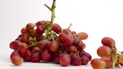 Juicy-red-grape-bunches-on-the-vine-falling-into-a-pile-on-white-table-top-in-slow-motion