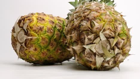 Two-whole-juicy-yellow-tropical-pineapples-falling-and-bouncing-on-white-table-top-in-slow-motion
