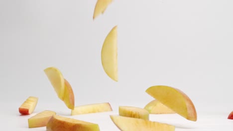 Sliced-red-and-yellow-fuji-apple-pieces-falling-onto-white-table-top-and-bouncing-into-a-pile-in-slow-motion
