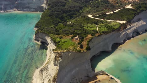 Breathtaking-drone-shot-of-Cape-Drastis-in-Corfu,-Greece-featuring-magnificent-sandy-cliffs-and-rock-formations,-pristine-Ionian-sea-and-lush-mediterranean-flora