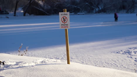 Schild-Warnt-Die-Menschen,-Nicht-Auf-Eis-Zu-Treten,-Mit-Menschen-Auf-Eis-Im-Hintergrund