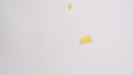 Bright-yellow-pineapple-fruit-cubed-pieces-raining-down-on-white-backdrop-in-slow-motion