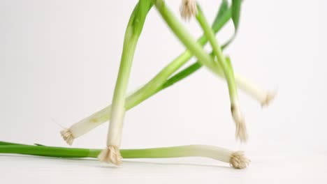 Green-scallion-onions-landing-and-bouncing-on-white-table-top-in-slow-motion