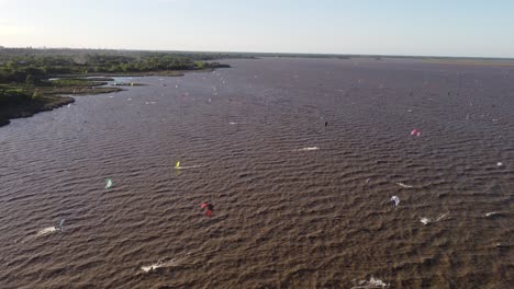 Luftüberführung-Welliger-Fluss-Mit-Vielen-Kitesurfern,-Die-An-Sonnigen-Tagen-In-Argentinien-Auf-Stürmischem-Wasser-Surfen