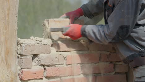 Worker-on-deconstruction-site-cleans-brick-from-mortar-with-hammer