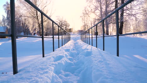 Snow-covered-metal-bridge-ahead-leads-towards-sunlight-on-cold-winter-morning