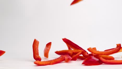 Sliced-julienned-red-bell-pepper-vegetable-pieces-falling-onto-white-table-top-into-a-pile-in-slow-motion