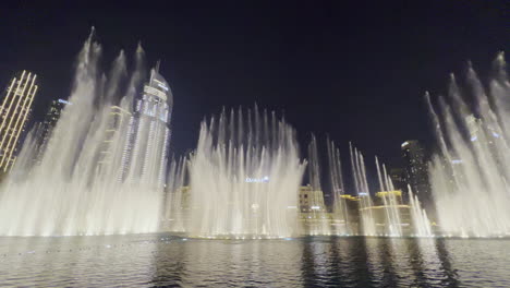Die-Wassershow-Von-Dubai-Brunnen-Bei-Nacht-Mit-Dem-Stadtbild-Als-Hintergrund