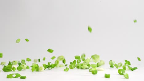 Diced-and-chopped-green-onion-pieces-falling-and-bouncing-onto-white-table-top-in-slow-motion
