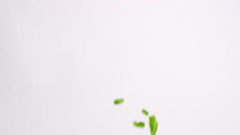 Bright-green-chopped-bell-pepper-vegetable-cubes-raining-down-on-white-backdrop-in-slow-motion