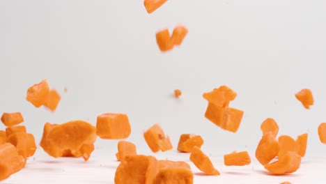Bright-orange-cubed-sweet-potato-pieces-falling-and-bouncing-onto-white-table-top-in-slow-motion