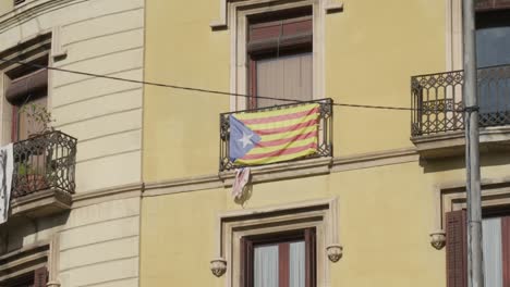 Bandera-De-Cataluña-Levantada-En-El-Balcón-Del-Edificio-En-La-Ciudad-De-Barcelona,-De-Mano