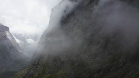Winding-road-passing-thru-the-mountains,-fog,-and-clouds-in-Milford-Sound-New-Zealand-on-the-South-Island