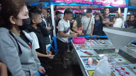 A-dynamic-handheld-footage-within-a-local-Filipino-fun-fair-playing-bets-on-six-cards-and-wins-the-round-whenever-the-tossed-ping-pong-balls-fall-into-the-card-you-placed-your-bet-on