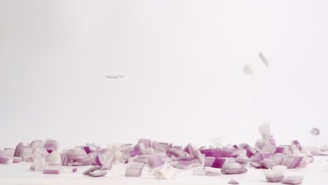 Chunks-of-cubed-chopped-red-onion-pieces-falling-on-white-table-top-in-slow-motion