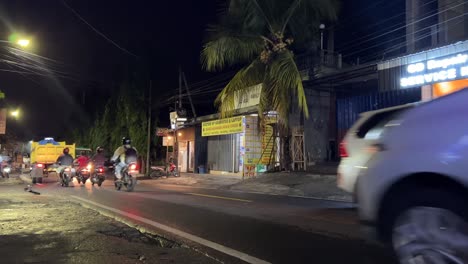 Road-Traffic-in-Bali-Street-with-local-shops-on-the-roadside-during-nighttime,-Static-shot
