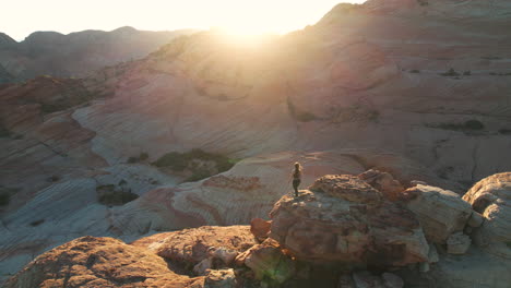 Aerial-View-of-Woman-Standing-on-Top-of-the-Rock-Above-Scenic-Desert-Landscape-at-Sunrise