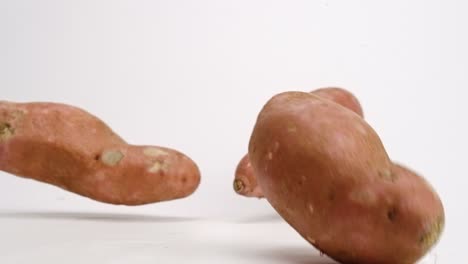 Whole-sweet-potato-root-vegetable-pieces-falling-and-bouncing-on-white-table-top-in-slow-motion