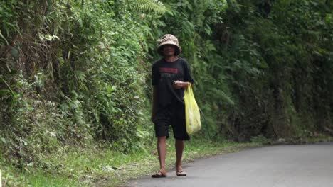 Ein-Lokaler-Balinesischer-Bauer,-Der-In-Zeitlupe-Die-Straße-Entlang-Geht-Und-Eine-Sense-Hält