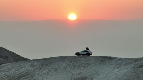 Man-sits-on-a-desert-hill-overlooking-a-sunrise-in-ontop-of-a-Mazda-car