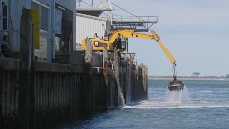 Yellow-excavator-working-on-a-platform-pulling-stuff-out-of-the-sea-in-slowmotion