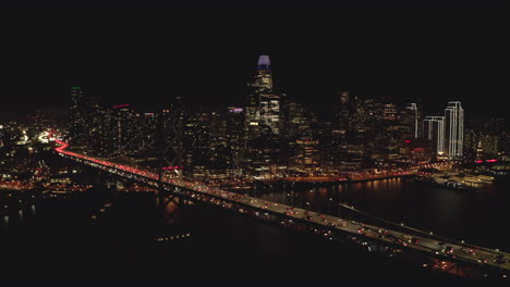 Circling-aerial-shot-of-Downtown-San-Francisco-skyscrapers-from-Bay-bridge-at-night