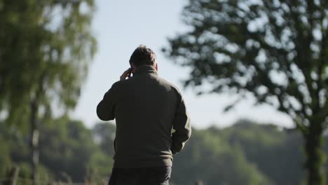 A-caucasian-farmer-calling-on-the-phone-in-the-nature-surrounded-by-trees-in-slowmotion