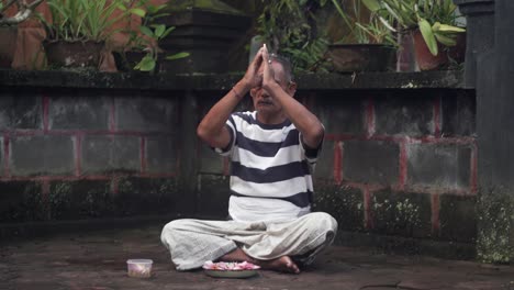 Portrait-of-Balinese-male-praying-with-hands-at-forehead,-Sitting-outside-of-Hindu-Temple