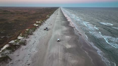 Vehicles-Driving-Through-The-Sandy-Shore-Of-Padre-Island-In-Texas,-USA---aerial-drone-shot