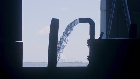 Large-amount-of-water-that-is-sprayed-from-a-pipe-in-a-fishing-factory-in-silhouette-slowmotion