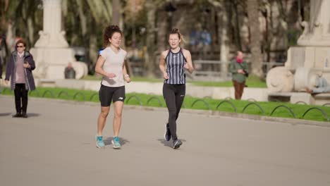 Female-friends-jog-in-Barcelona-city-on-sunny-warm-day,-slow-motion
