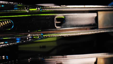 A-stylized-and-dramatic-panning-close-up-of-the-inside-of-a-stapler-loaded-with-staples-illuminated-by-a-blue-and-green-light-with-black-background