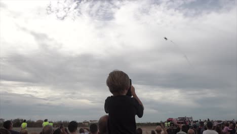 Crowd-of-spectators-airplane-show,-a-Boy-on-his-father's-shoulder-recording-stunts-on-a-smartphone,-Slow-motion