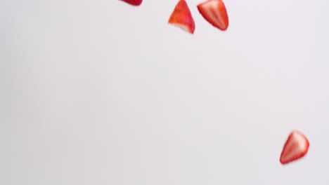 Bright-red-strawberry-half-pieces-raining-down-on-white-backdrop-in-slow-motion