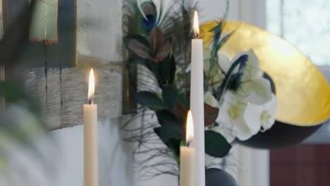 Langsame-Aufschlussreiche-Aufnahme-Von-Brennenden-Kerzen,-Die-Auf-Einem-Tisch-Hinter-Grünen-Blättern-Brennen